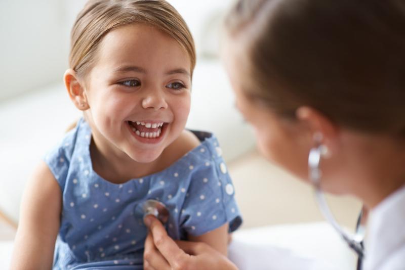 a young girl smiling as a medical provider listens to her heart with a stethoscope